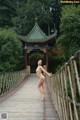 A naked woman standing on a wooden bridge.