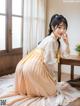 A woman in a yellow and white hanbok sitting on a bed.