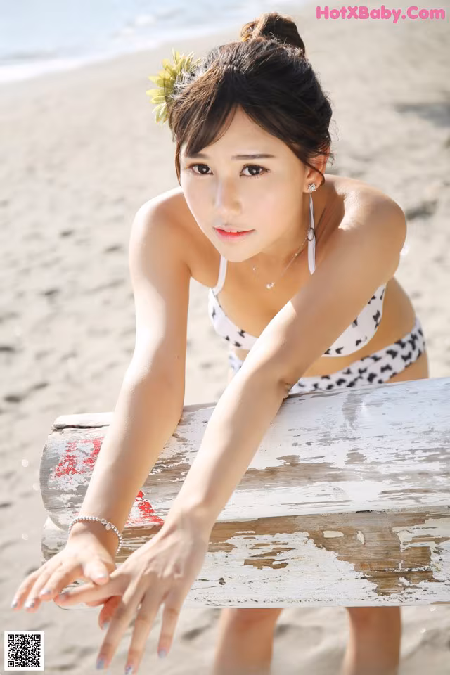 A woman in a bikini sitting on a bench on the beach.