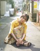 A woman sitting on the ground in a yellow shirt and colorful pants.