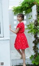 A woman in a red dress leaning against a white wall.