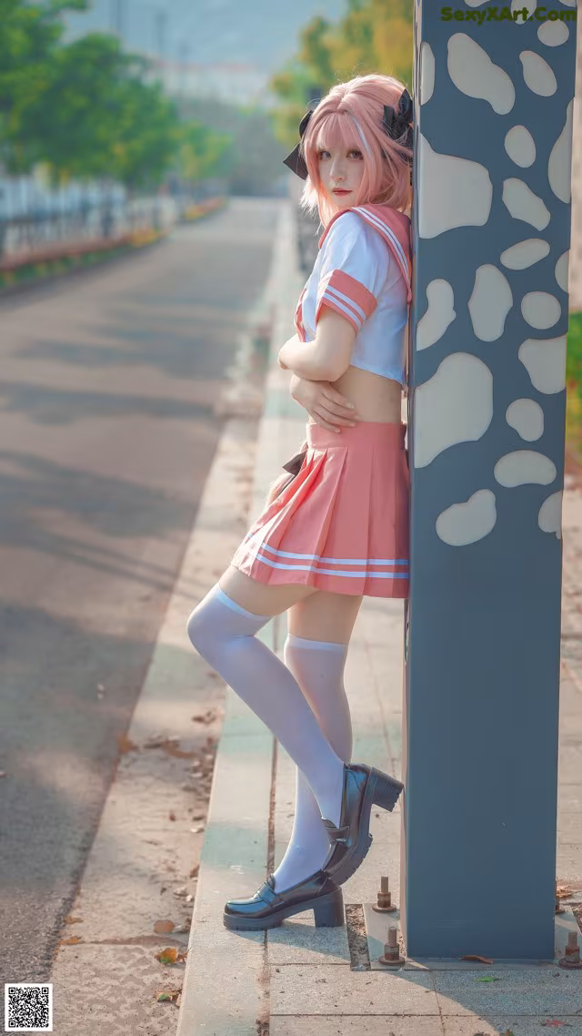 A woman in a pink and white outfit leaning against a pole.