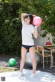 A woman in a white shirt and blue shorts holding a pink ball.