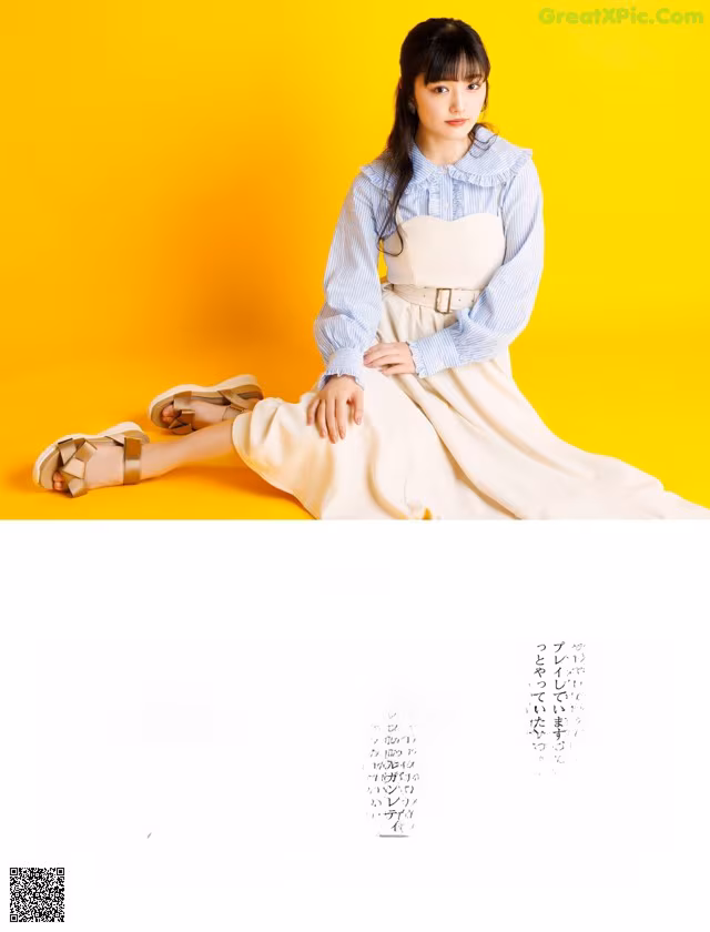 A woman sitting on a yellow background wearing a white dress.