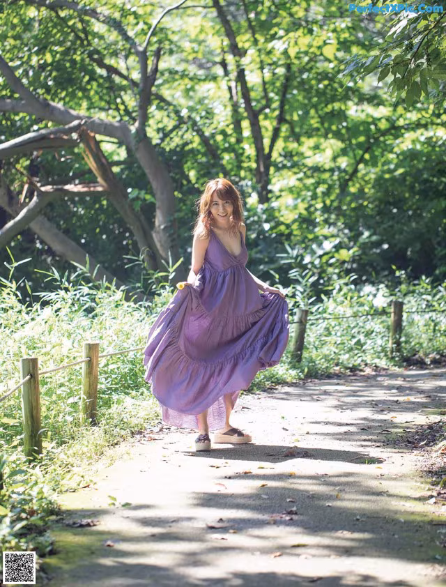 A woman in a purple dress walking down a path in the woods.