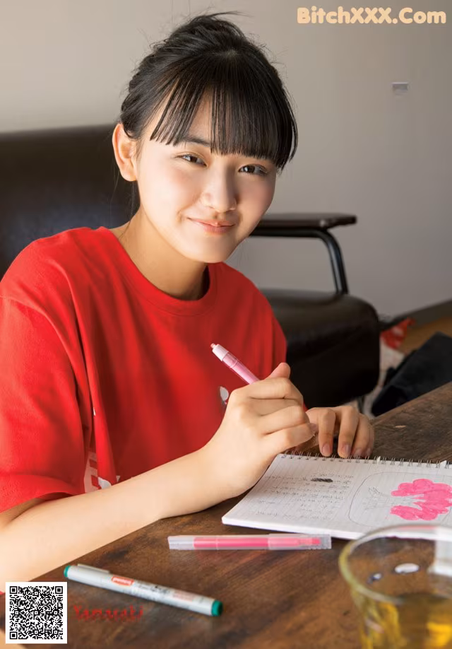 A young woman sitting at a table writing in a notebook.