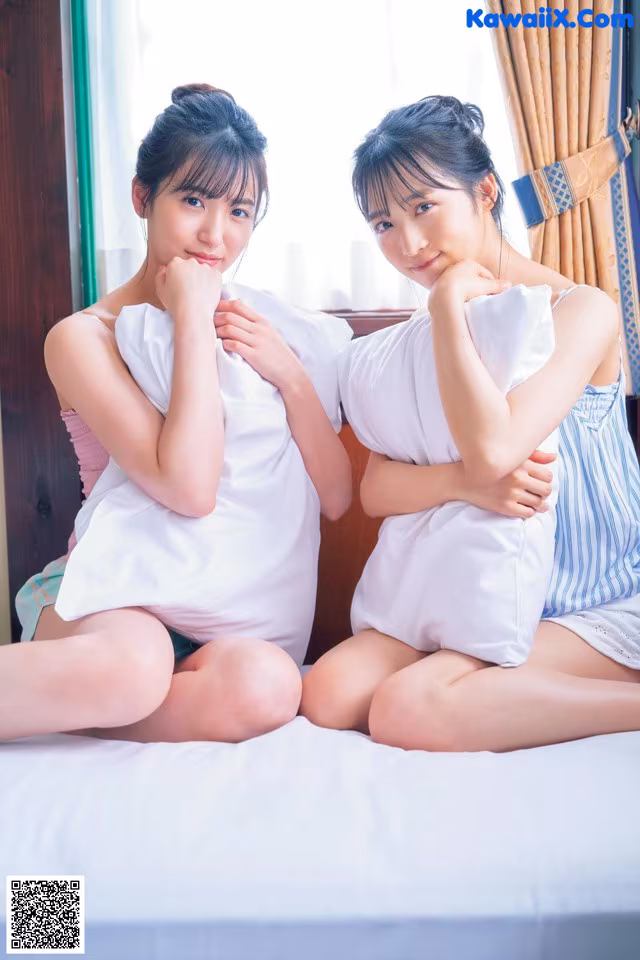Two young women sitting on a bed with pillows.