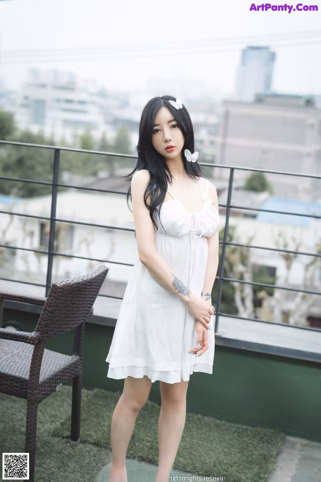 A woman in a white dress standing on a balcony.
