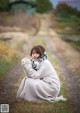 A woman sitting on a dirt road wrapped in a blanket.