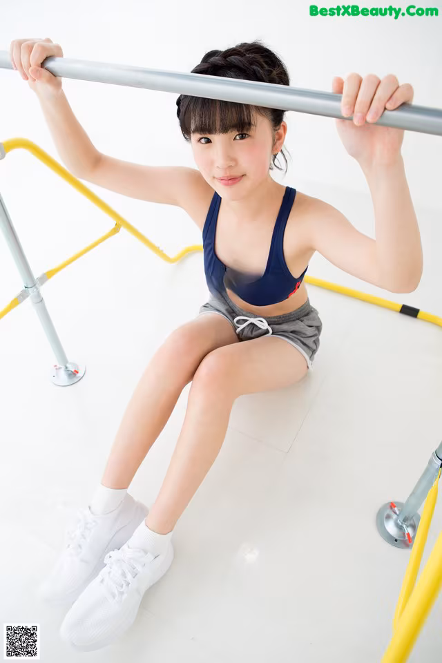A young woman is sitting on a bar in a gym.