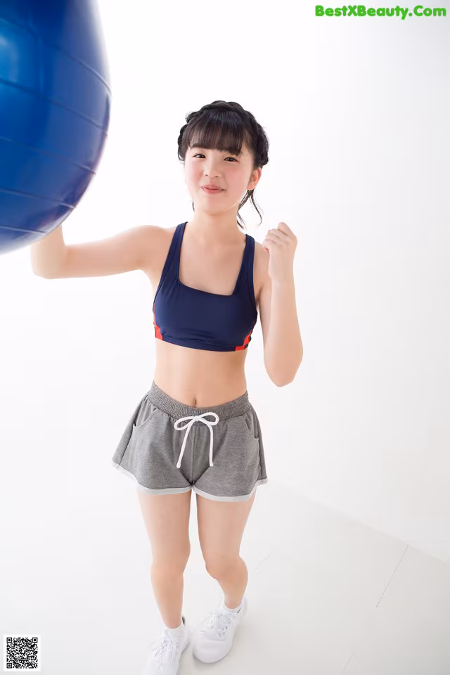 A woman in a sports bra top and shorts holding a blue ball.