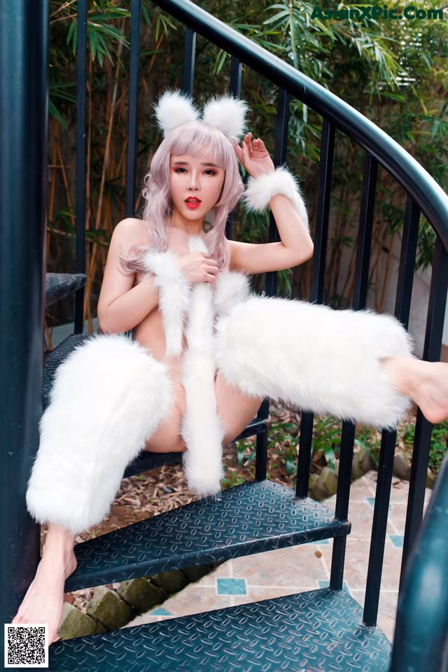 A woman in a white fur coat sitting on a set of stairs.