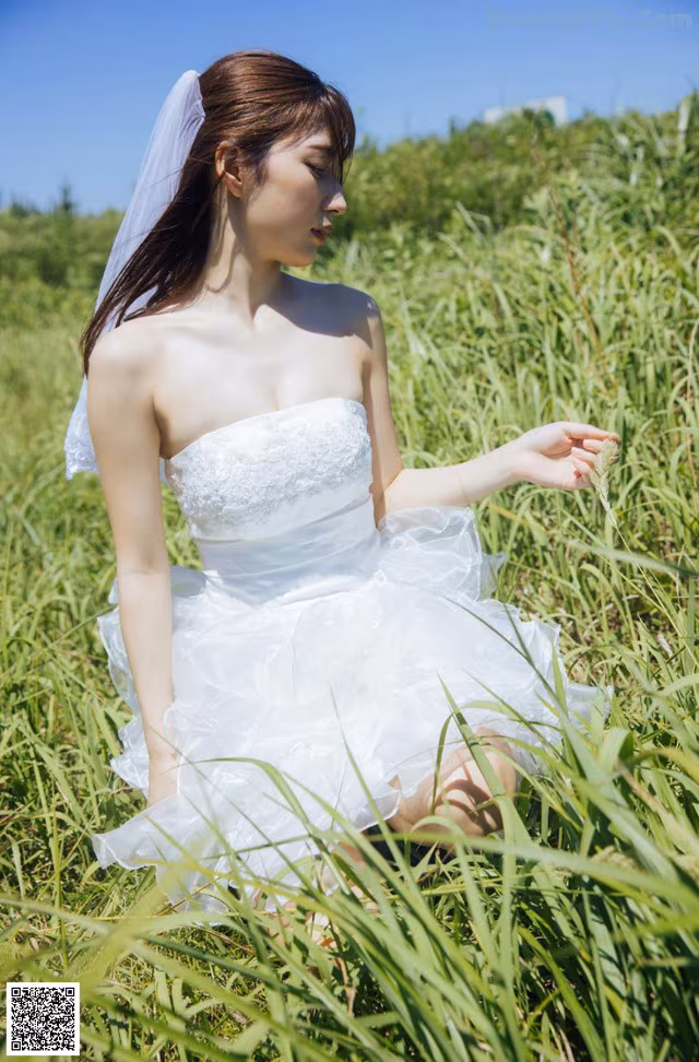 A woman in a wedding dress sitting in tall grass.