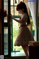 A girl in a white dress standing by a window.