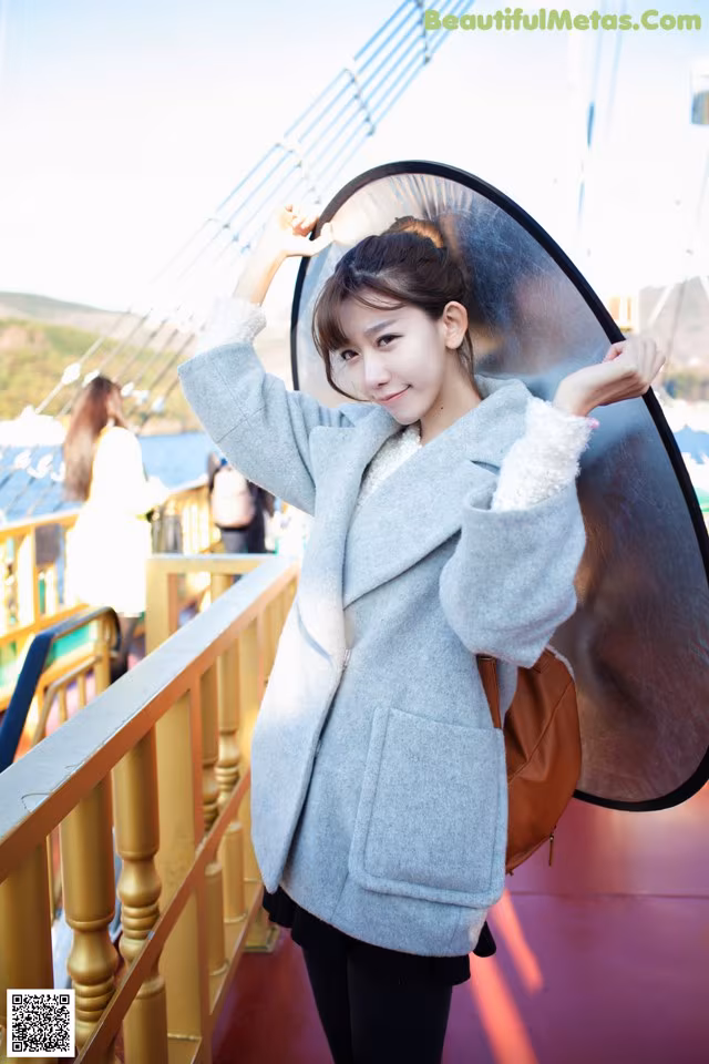 A woman in a gray coat holding a large umbrella.