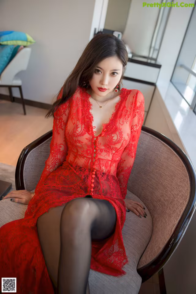 A woman in a red dress sitting on a chair.